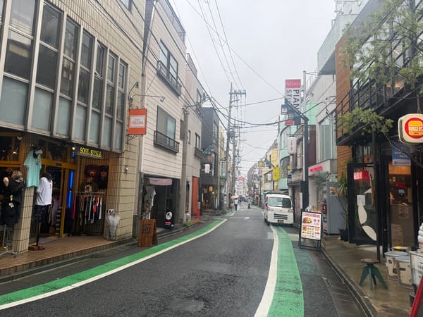 下北澤一番街的窄巷，地上畫著綠色自行車道，一邊掛著衣架，對面立著午餐菜單看板
